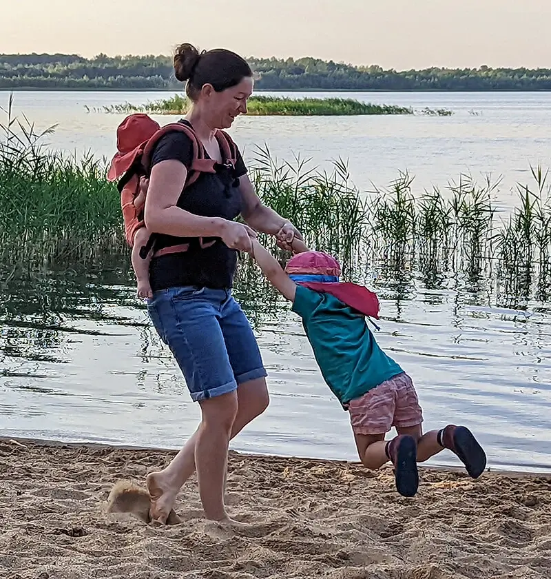 Mama mit Baby in der Trage auf dem Rücken und Kind an den Händen am Strand · Abenteuer Bindung · Sandra Bäthge in Magdeburg